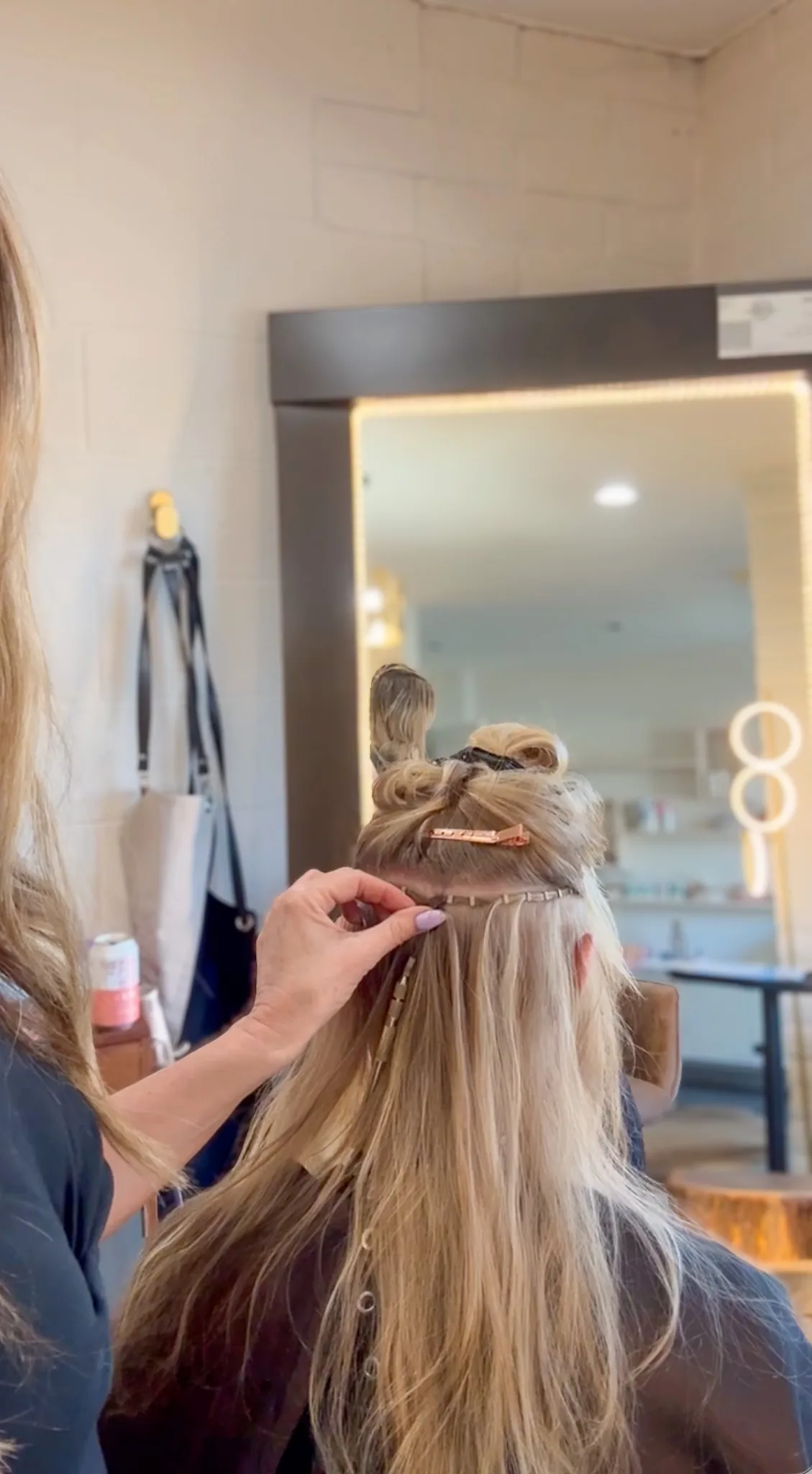 Alisa working along a beaded row at the back of a blonde client's head, the top section clipped up.