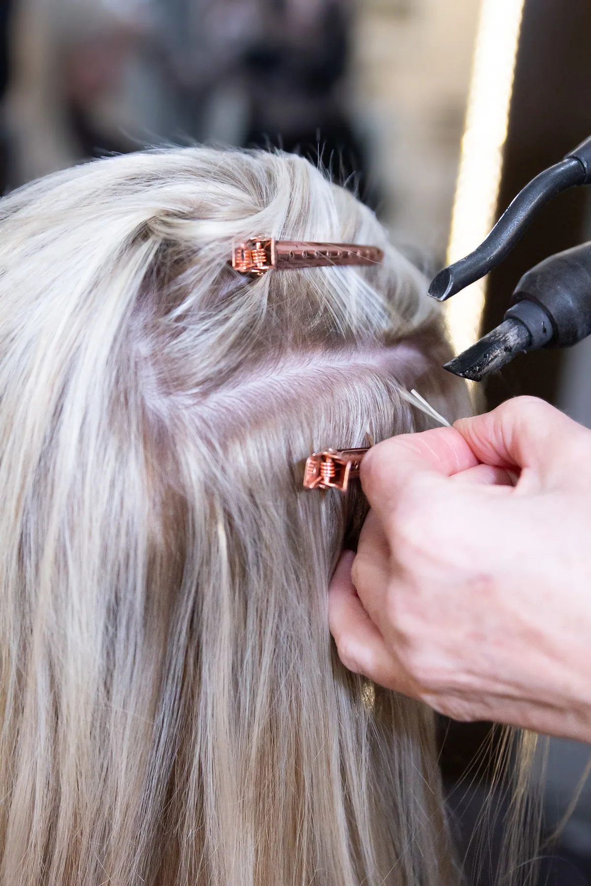 A keratin bond being fused onto a fine section of pale blonde hair, the fusion tool held just above it.