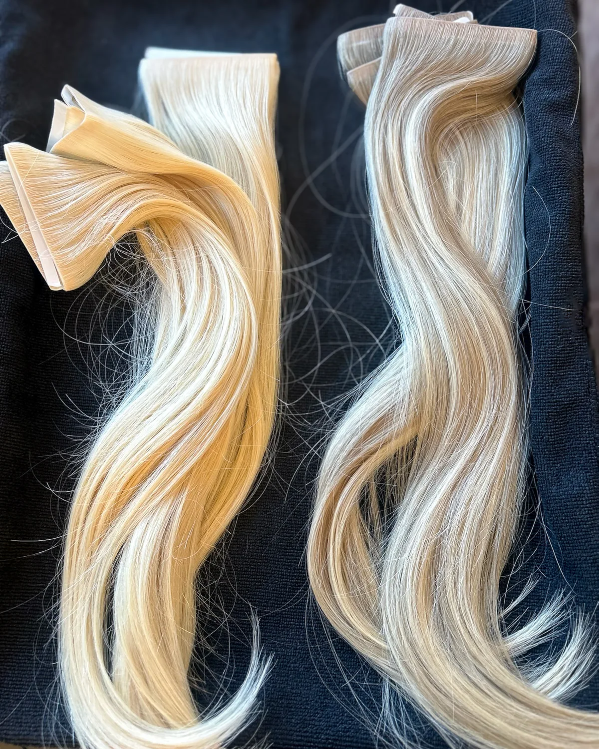 Two blonde tape wefts laid out on black, the adhesive tabs along the top of each.