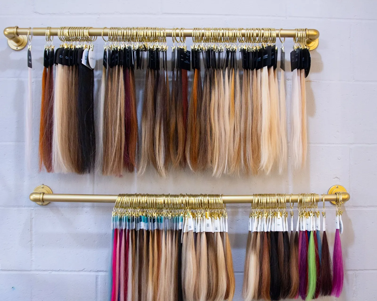 Rows of hair color swatches hanging from brass rods on a white brick wall.